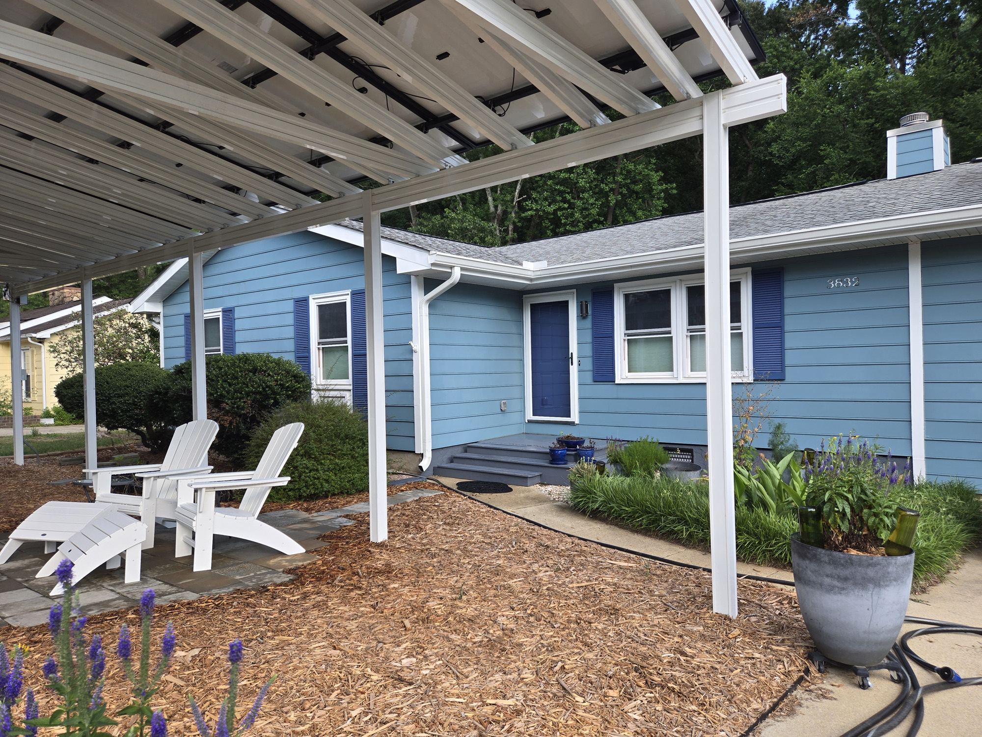 A blue ranch home with a solar pergola and clean patio — the kind of full-property refresh that pairs house washing with hardscape and panel cleaning.